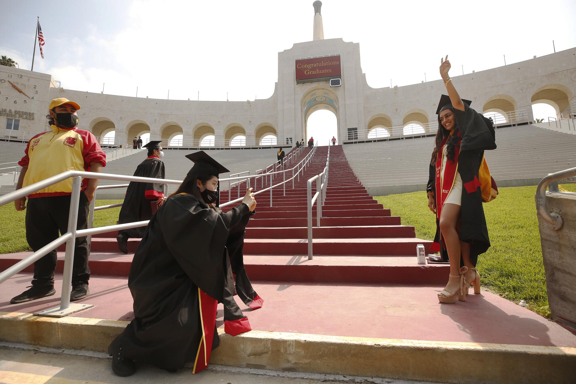 A student kneels to take a photo of another student holding up her hand in a V shape in front of the Coliseum's Olympic torch