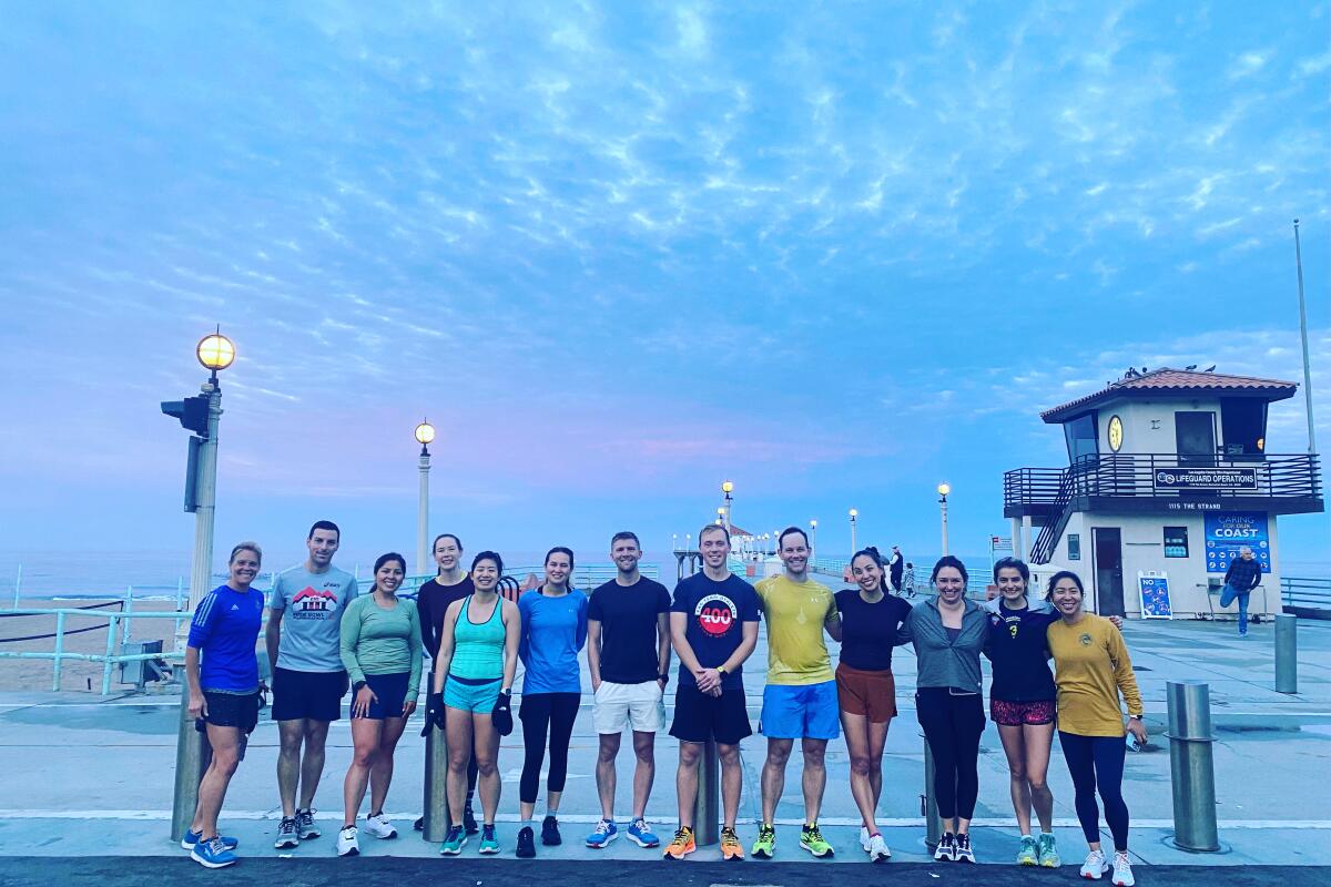 A line of runners on a beach path with a lifeguard tower behind, under an overcast dawn sky