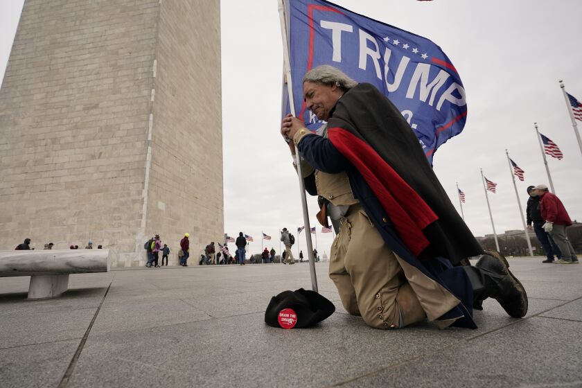 A man dressed as George Washington kneels and prays near the Washington Monument with a Trump flag 
