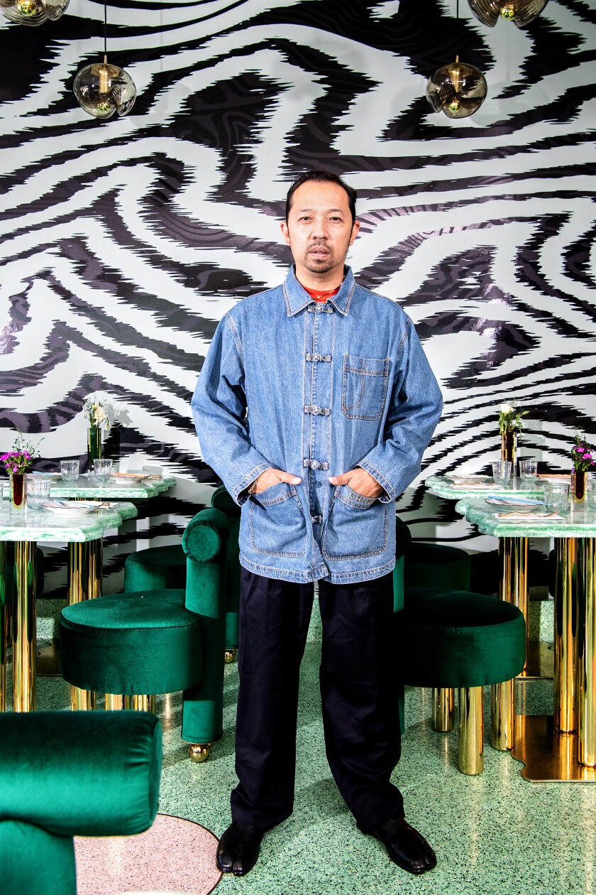 A man in a denim smock in front of a black-and-white striped wall in a restaurant.