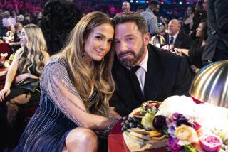 A woman and man in formalwear lean their heads together while sitting at a table with florals on it