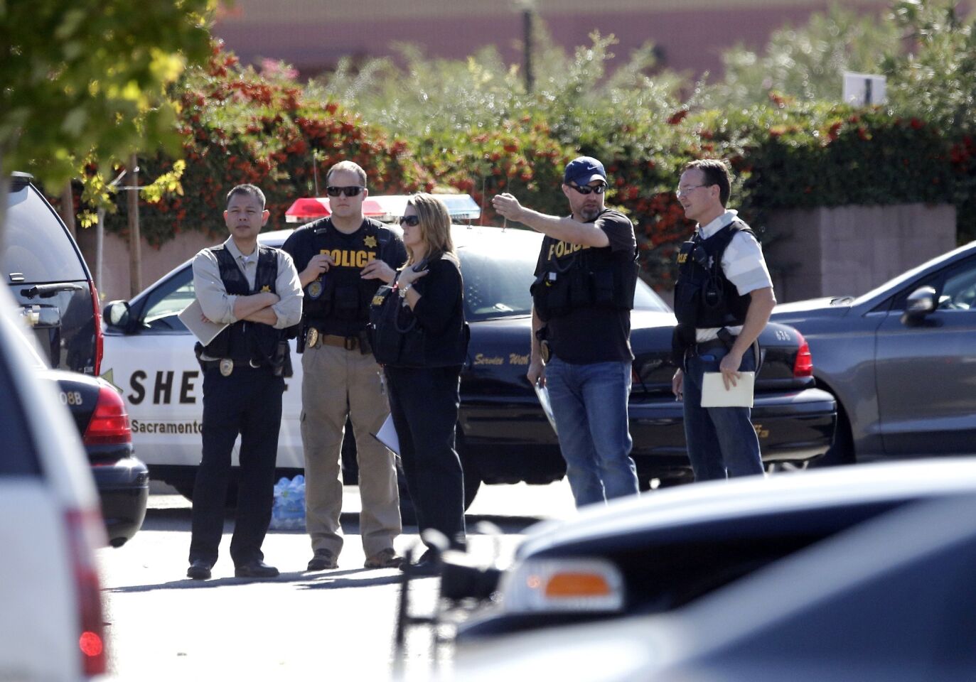 Law enforcement officers gather at the site where a Sacramento County sheriff's deputy was fatally shot by an assailant who then allegedly carjacked two vehicles and prompted a manhunt that ended with two other deputies wounded, one mortally, along with a motorist.