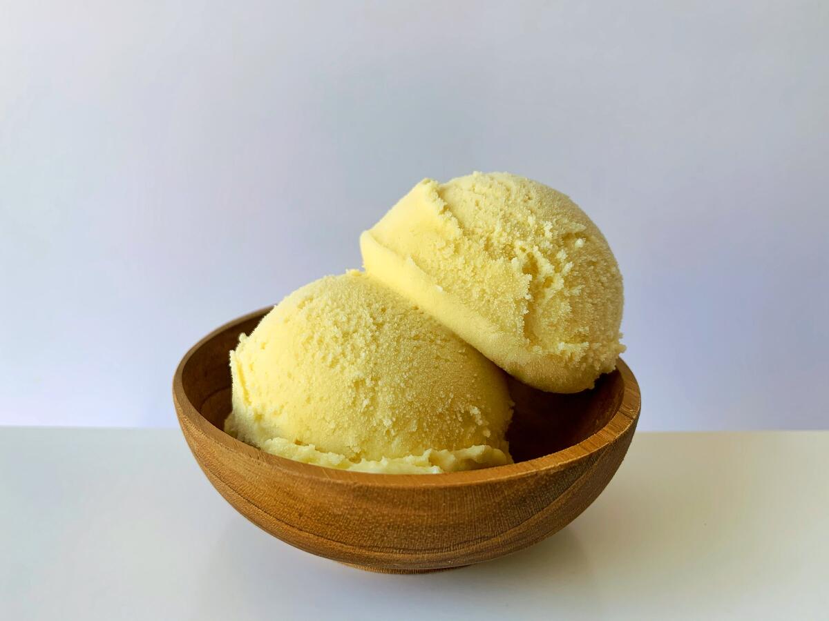 A wooden bowl on a white table with two scoops of vanilla ice cream.
