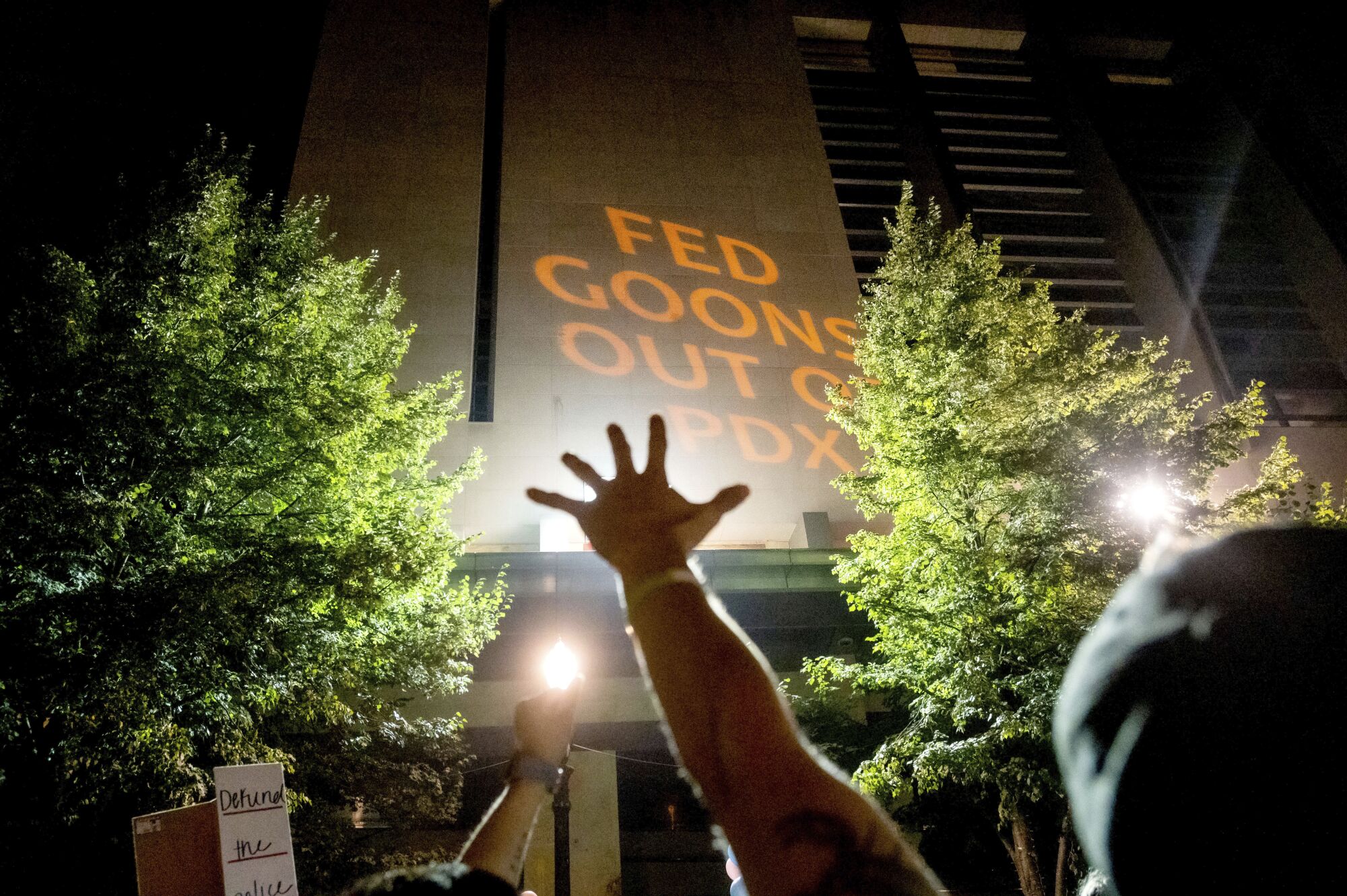 A protester raises his hand as text is projected onto the courthouse.