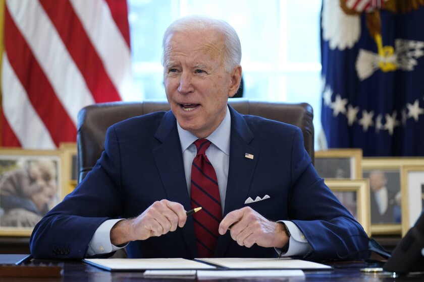 President Biden sits at his desk holding a pen