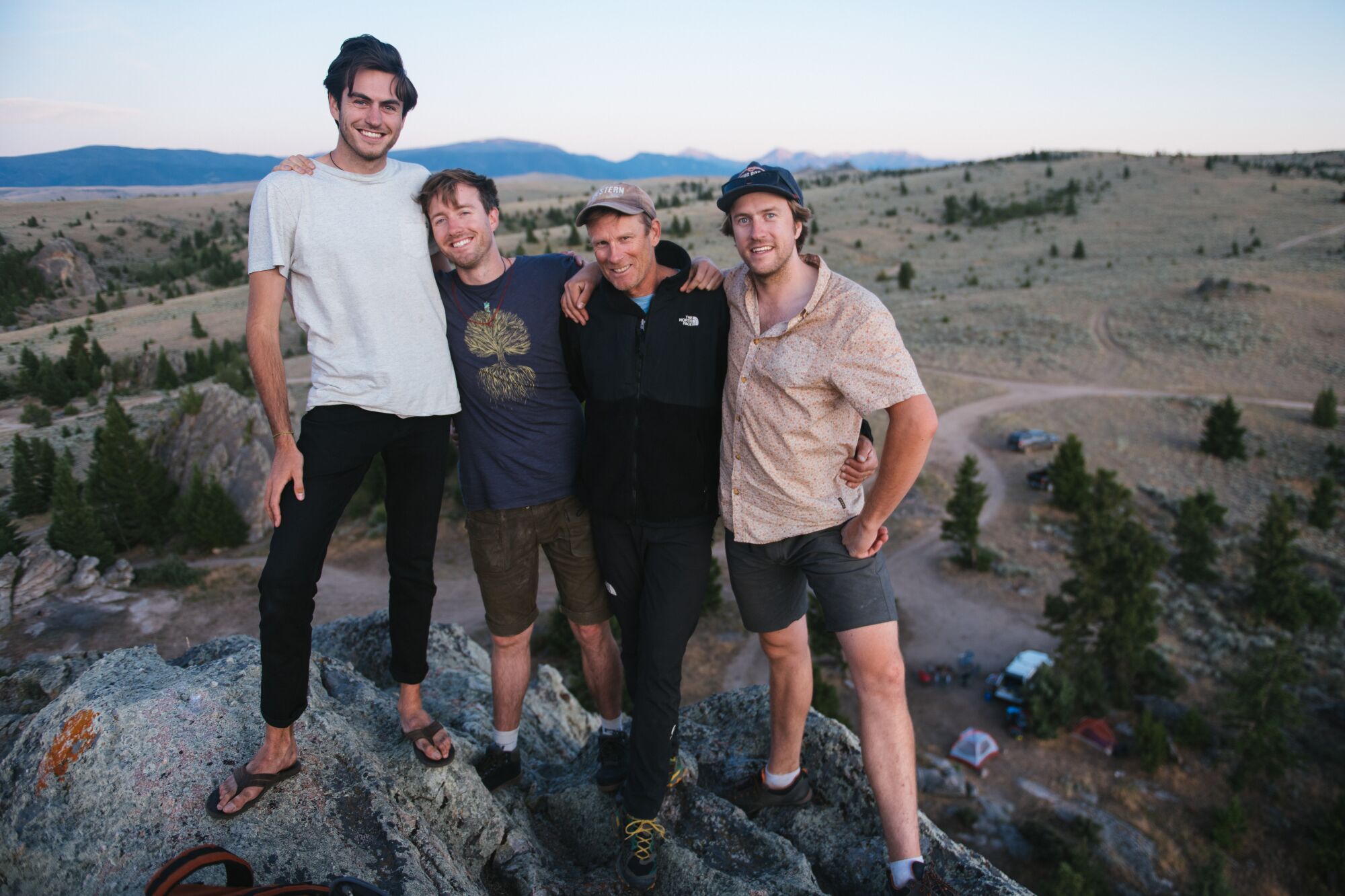 Four men stand together on a boulder with the landscape visible behind them.
