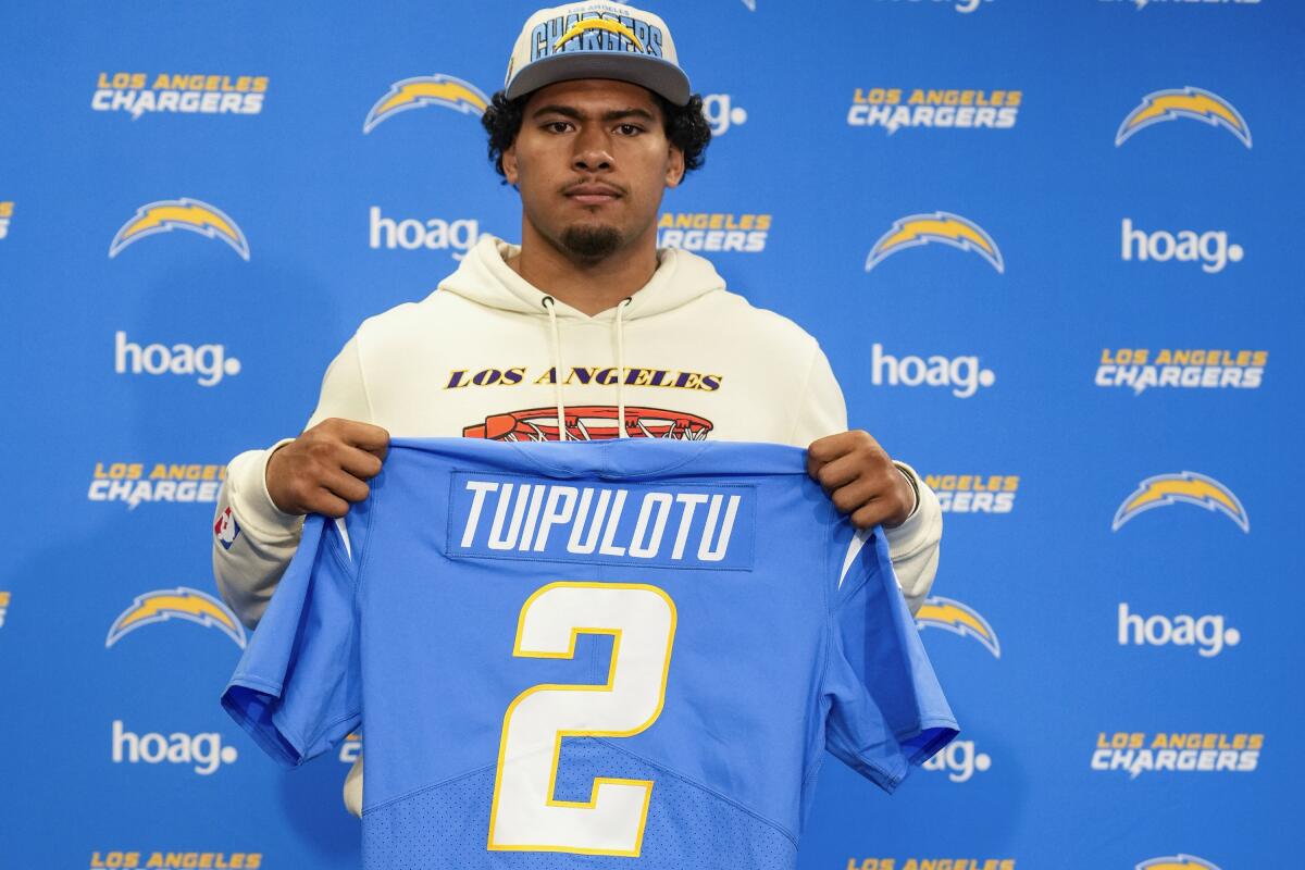 Tuli Tuipulotu poses with a Chargers jersey after the team selected him in the second round of the 2023 NFL draft.