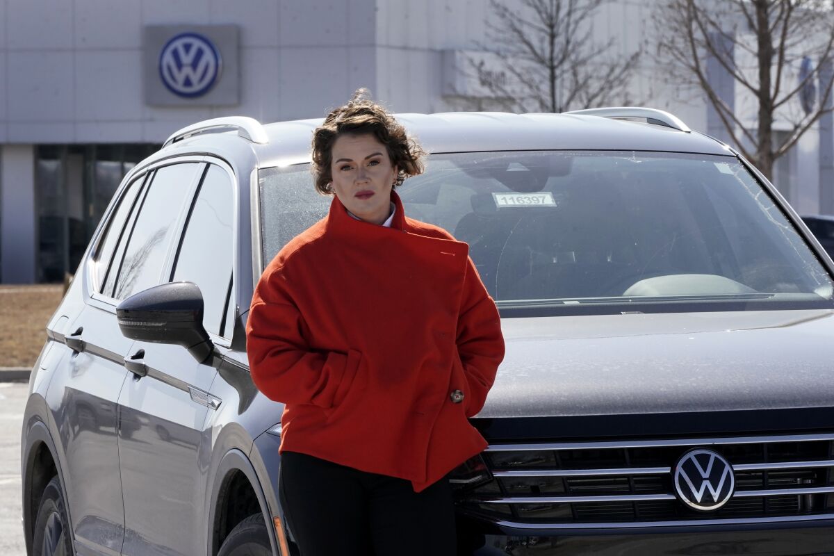 Kendall Heiman stands with the loner car she has driven for the past two months, Wednesday, March 9, 2022, in Lawrence, Kan., while a dealership works to repair her Volkswagen 2021 Atlas Cross Sport after the car slammed on the brakes for no reason on Jan. 5. Heiman and a dozen other Cross Sport owners have filed complaints about the issues with the U.S. National Highway Traffic Safety Administration. (AP Photo/Charlie Riedel)