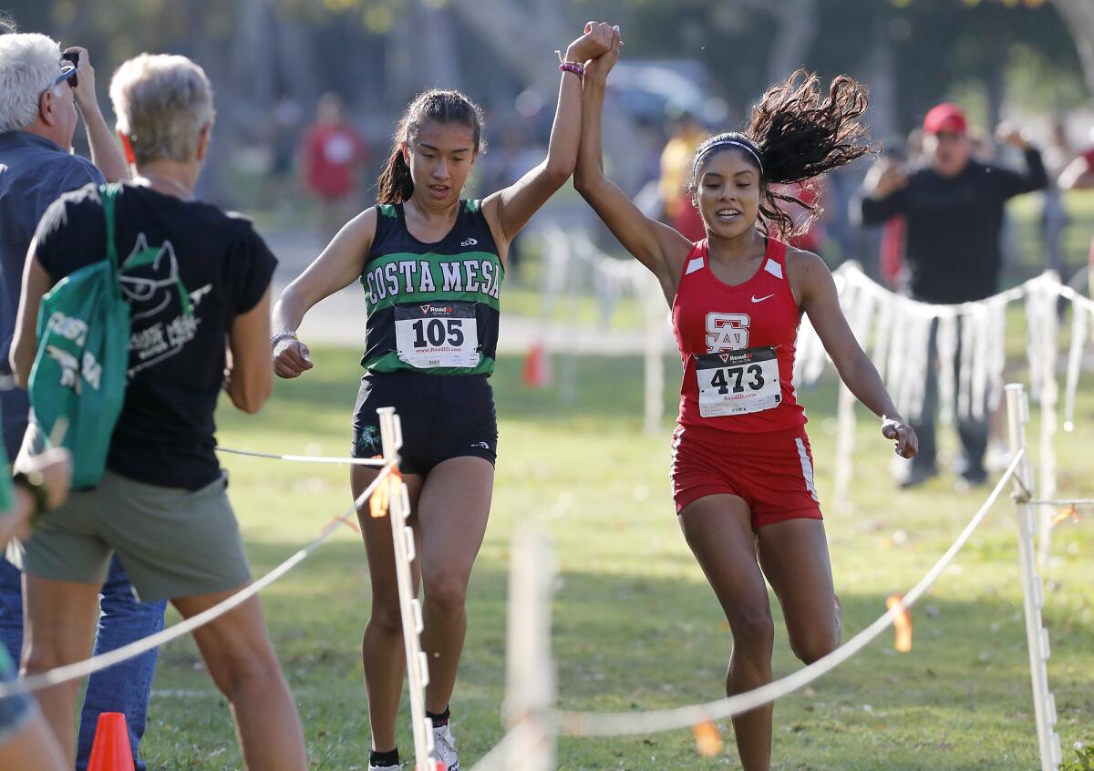 Costa Mesa’s Diane Molina, left, and Santa Ana’s Maria Hernandez hold hands after crossing the finish line in the Orange Coast League final at Irvine Regional Park in Orange on Nov. 5. Hernandez finished first with a time of 17:54.78 and Molina second in 17:55.04.