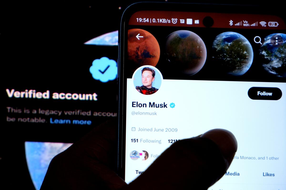 Elon Musk's Twitter account is displayed on a smartphone with a verified account in the background.