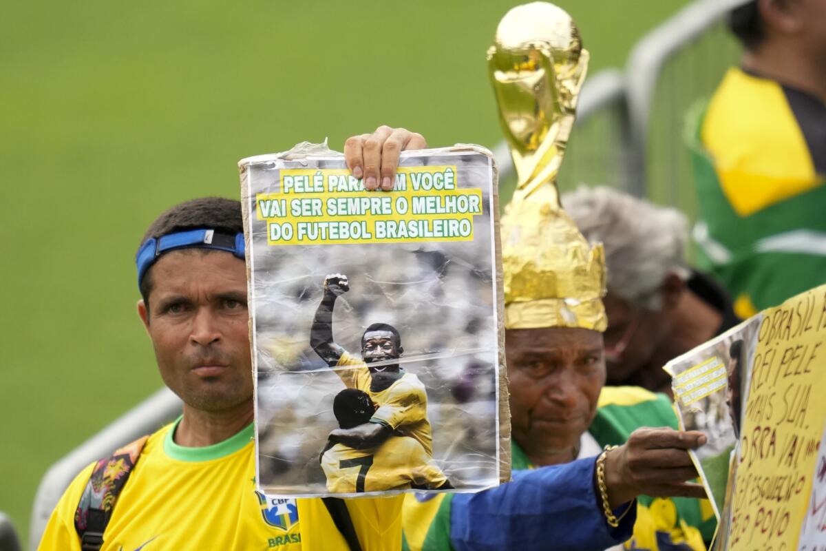 Fans hold photos of Pelé as they line up at Vila Belmiro stadium to file past his coffin.
