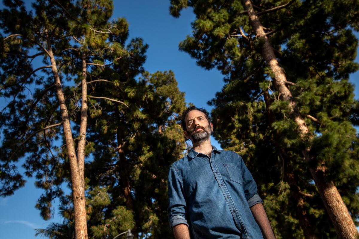 Dan O'Brien, in a denim shirt, stands amid a grove of Canary Island Pine trees.
