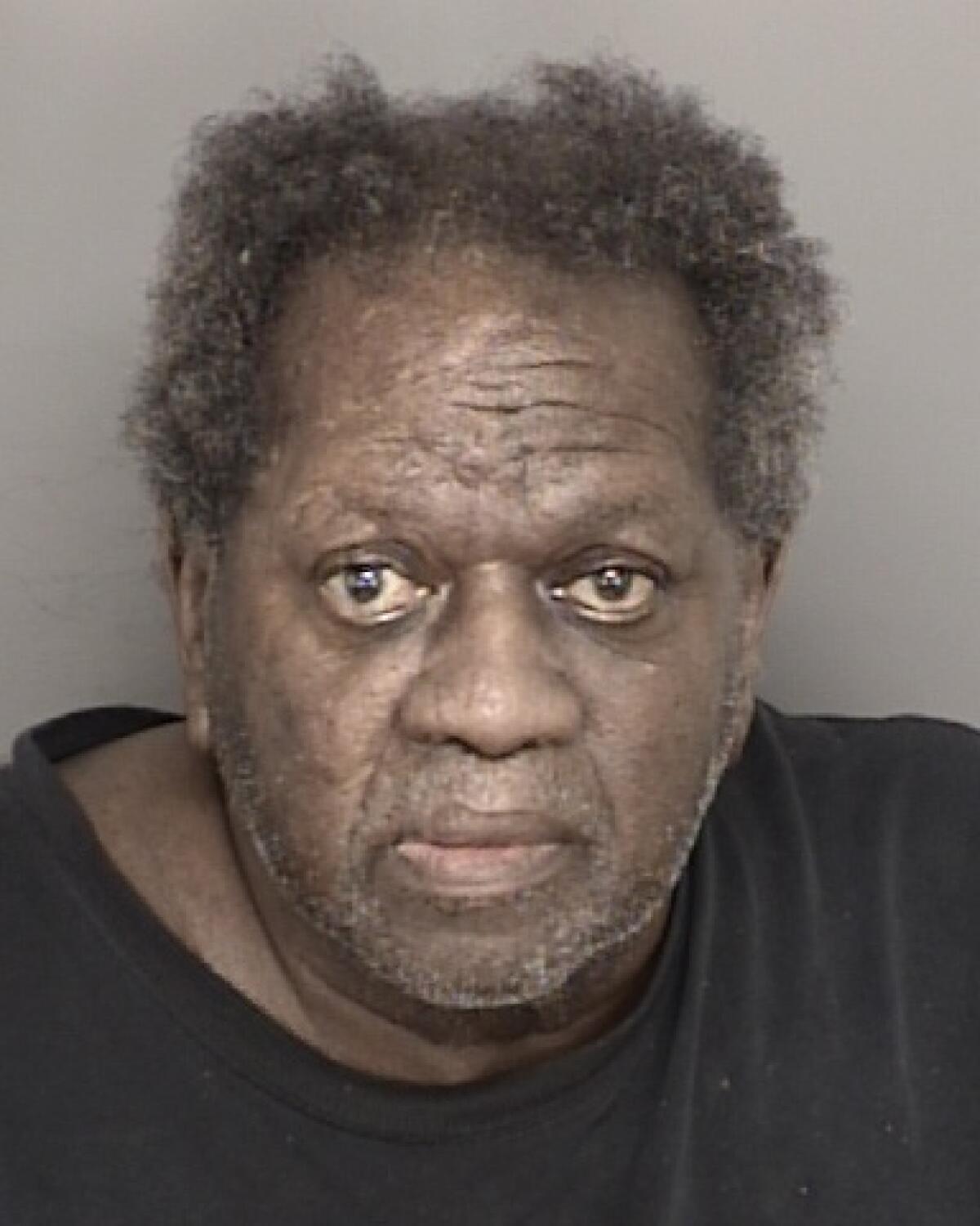 A man in a dark T-shirt and graying hair is shown in a mug shot.