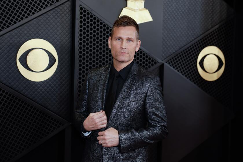 Kaskade wears a black shirt and holds the lapel of his metallic blazer while arriving at the Grammy Awards