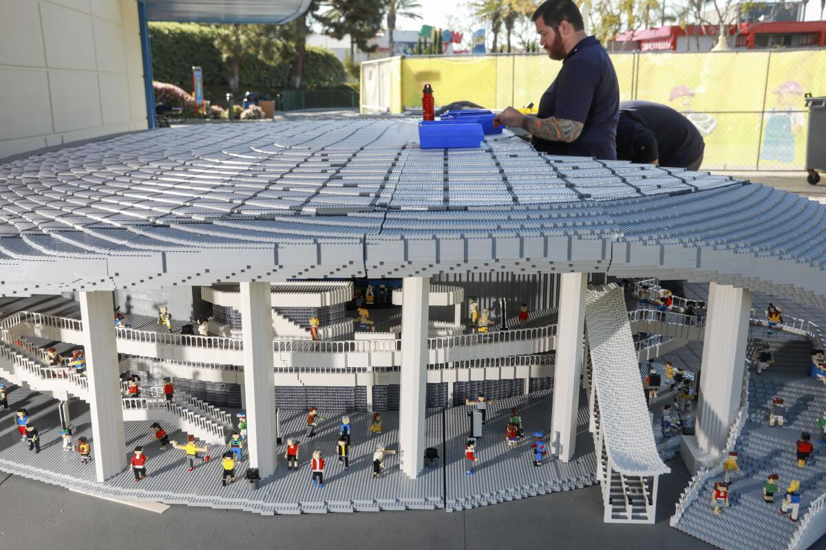 A man standing over a Lego replica of a stadium.