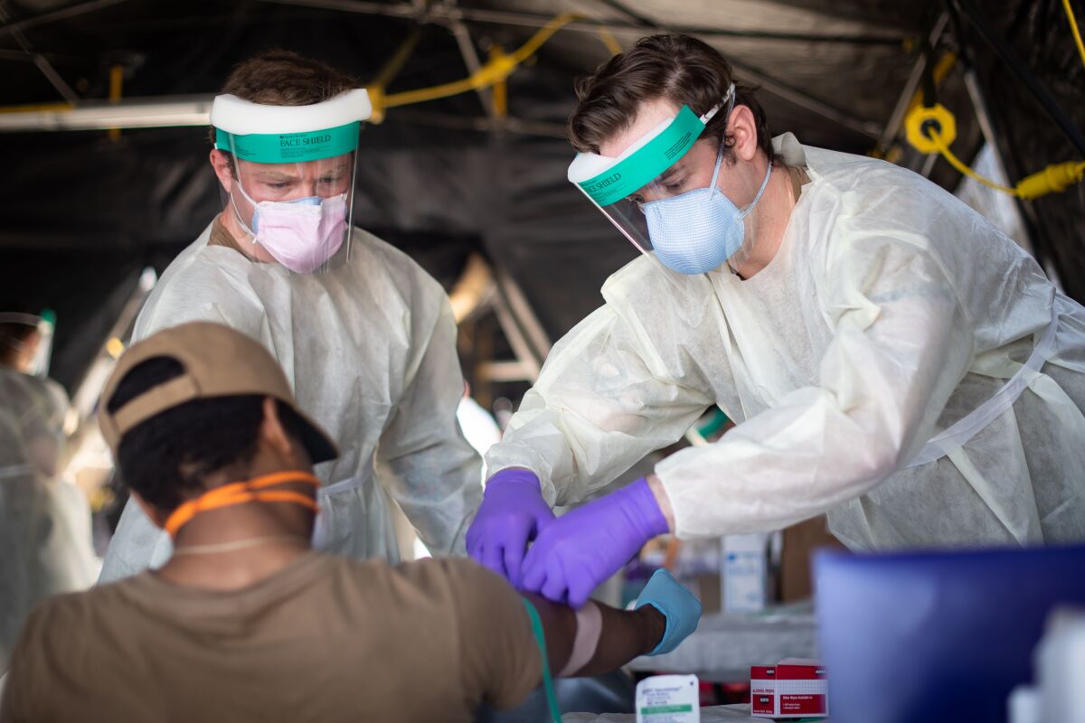 Hospital Corpsman 2nd Class Shane Miller, left, and Hospital Corpsman 2nd Class Austin Kelly, both assigned to Fleet Surgical Team 9, draw blood from a sailor assigned to the guided-missile destroyer Kidd after its arrival in San Diego last week.