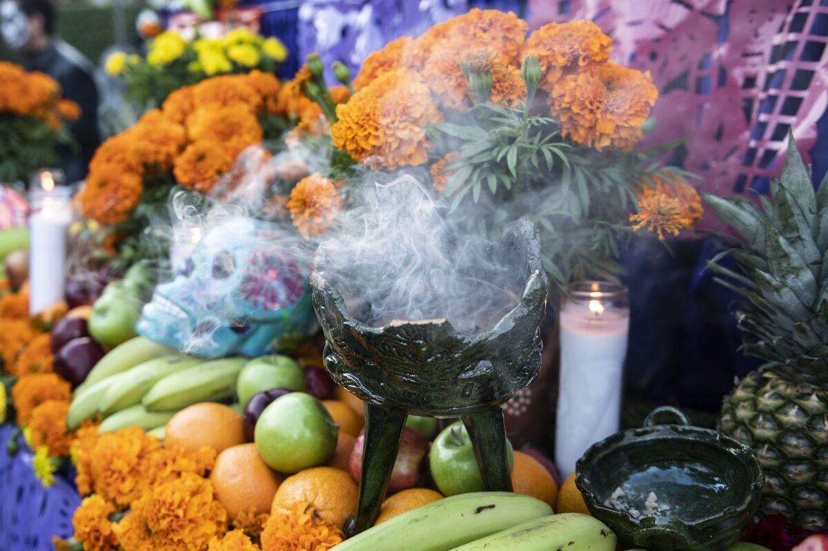 Incense burns on a Día de Muertos ofrenda decorated with fruits and marigolds