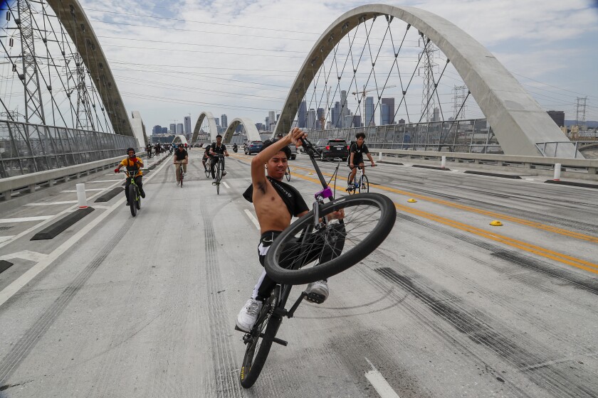 A young man pops a wheelie on his bicycle in the middle of a bridge.