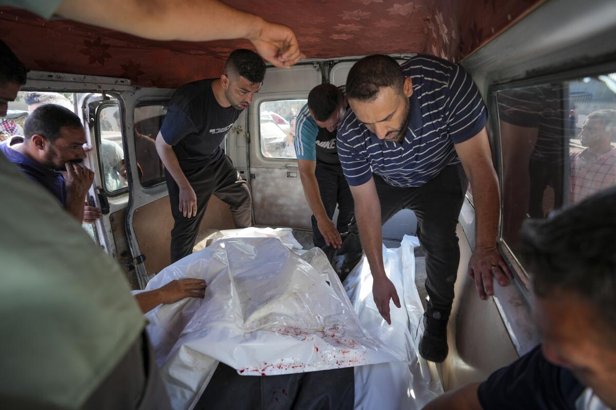 Palestinians move bodies covered in bloodied white sheets inside a vehicle. 