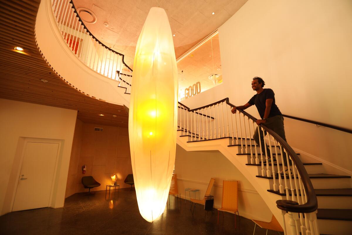 Rohan Silva stands on a curving staircase within view of a giant chandelier shaped like a cocoon.