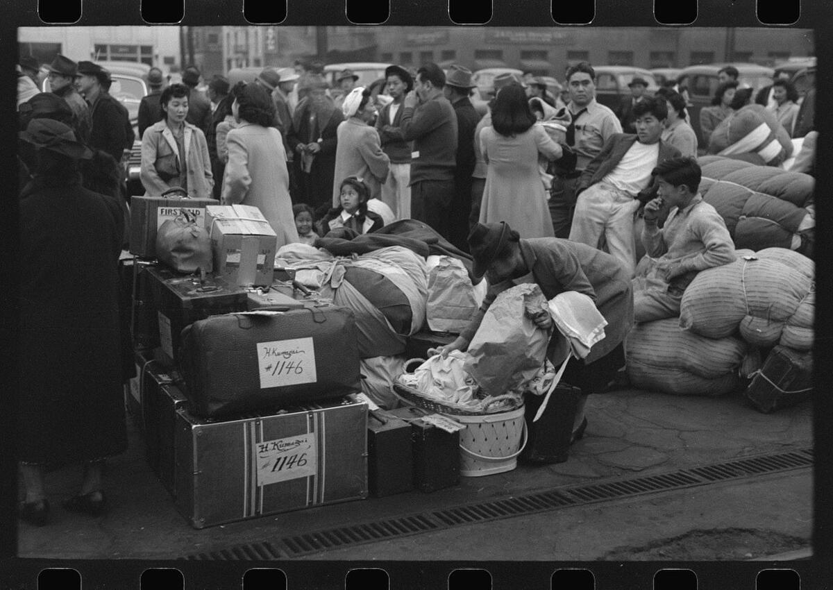 People wait with luggage at a rail station in a World War II-era photo