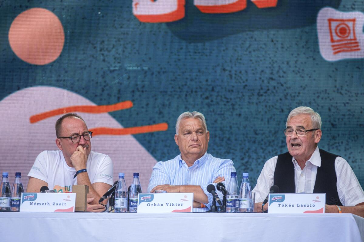 Three men sit at a table behind name markers and water bottles.