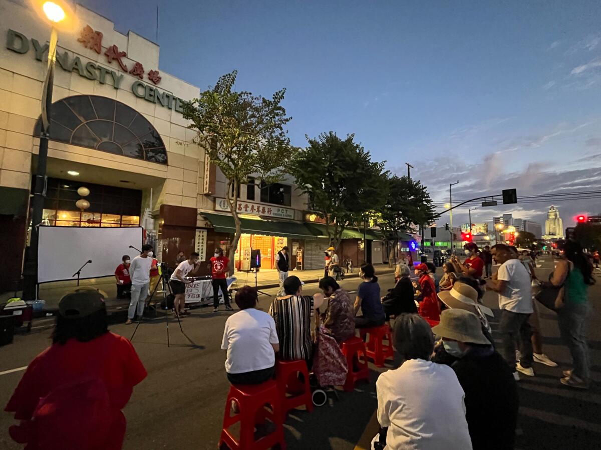 A seated audience looks at people in a central area outdoors.