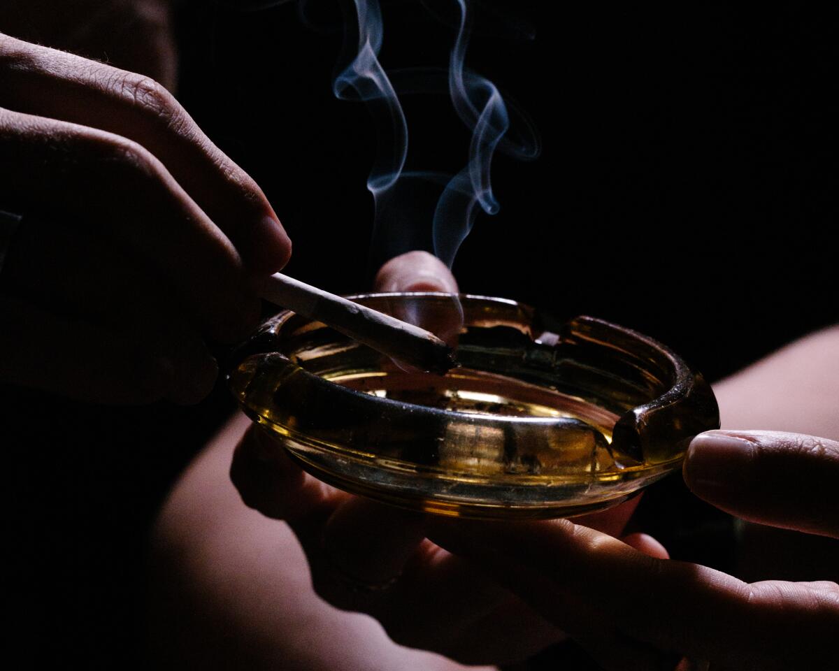 A marijuana joint smolders as someone holds it above an ashtray