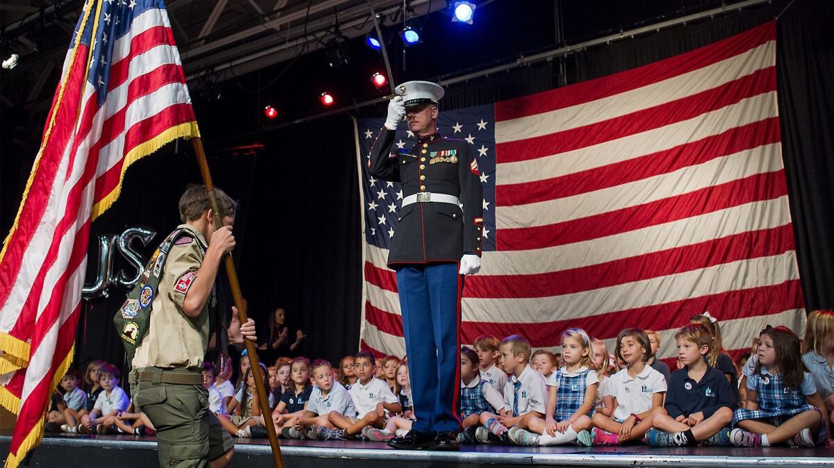 Retired U.S. Marine Dwight Hanson salutes as Boy Scout Sam Perkins carries the U.S. flag during a Veterans Day commemoration at Mariners Christian School in Costa Mesa on Nov. 11, 2016.