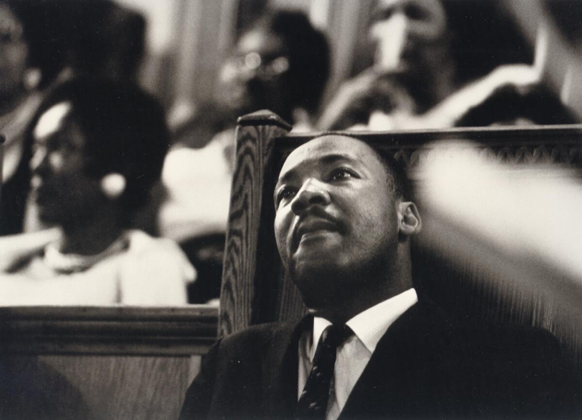 A black-and-white image of a man sitting on a wooden bench