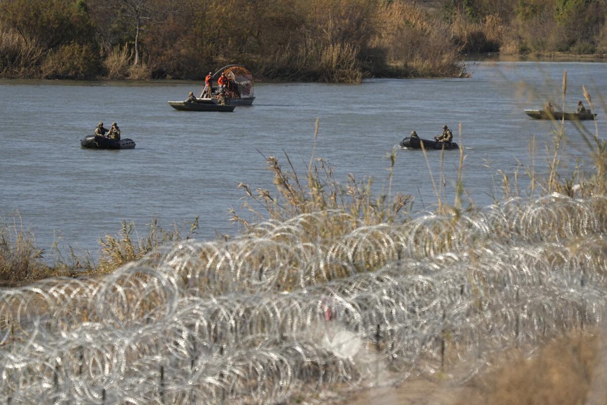 Boats are shown in a river, with concertina wire in the foreground.