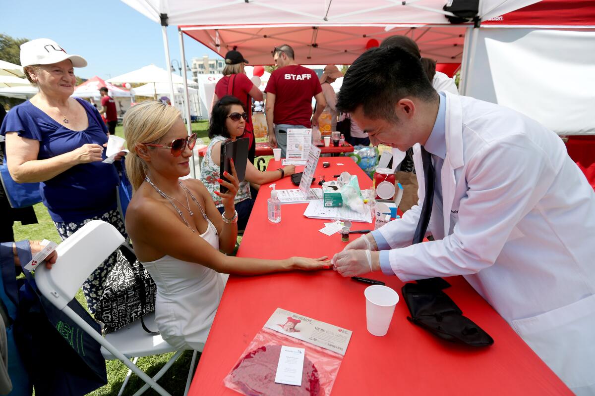 Rosario R. of Glendale gets her blood sugar checked by pharmacy resident Marc Salvatus at the Adventist Health Glendale and American Heart Association-sponsored Wellbeing Block Party at Central Park in Glendale on Aug. 24.