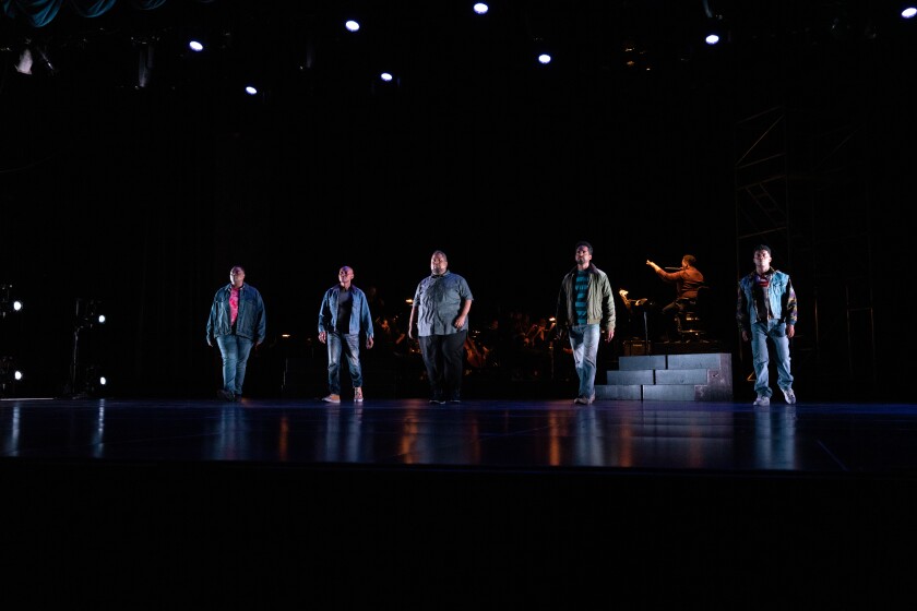 Cinco cantantes de ópera repartidos en un escenario oscuro.