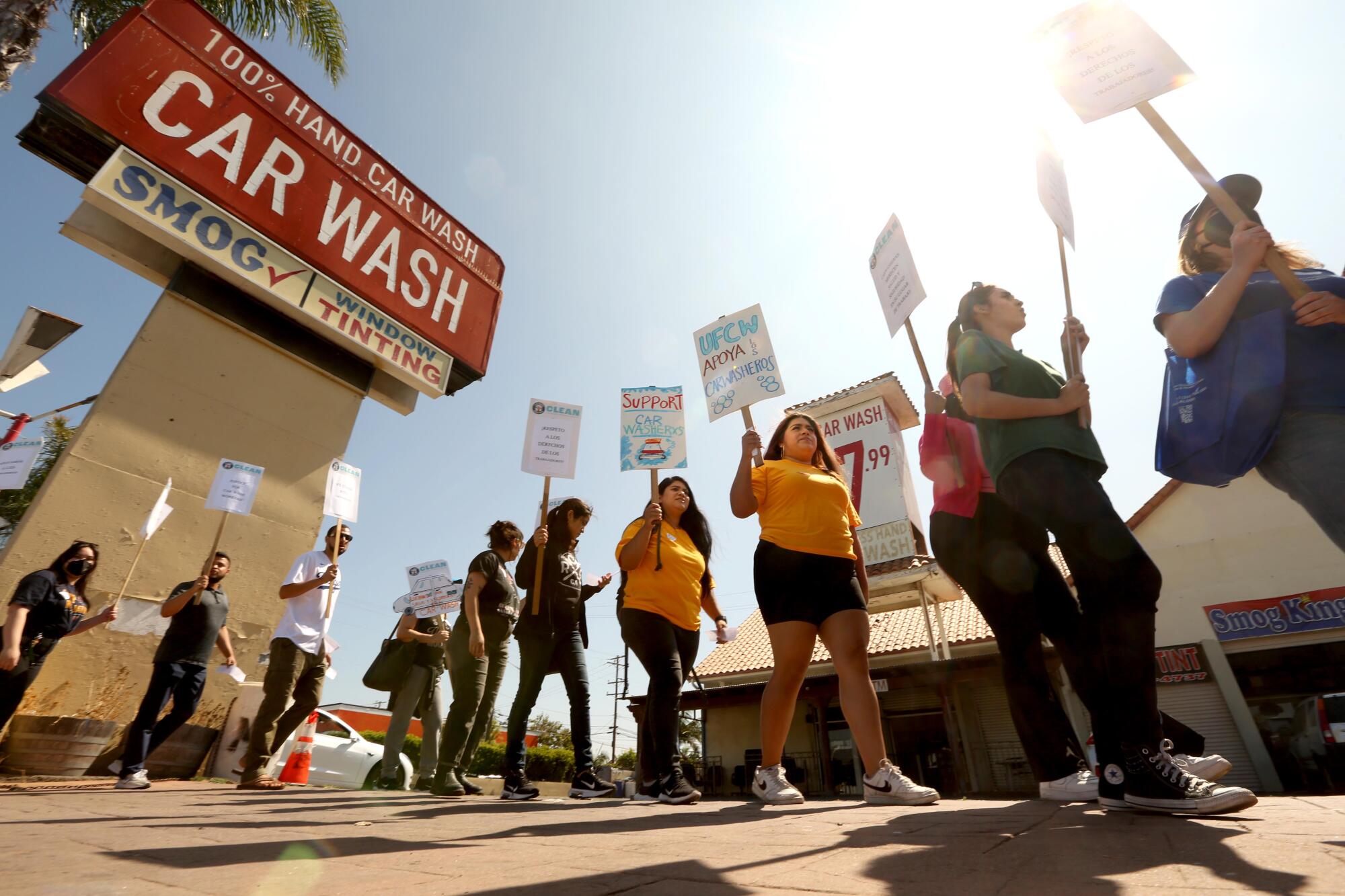 Two UCLA students in yellow shirts walk a picket line at a carwash. 