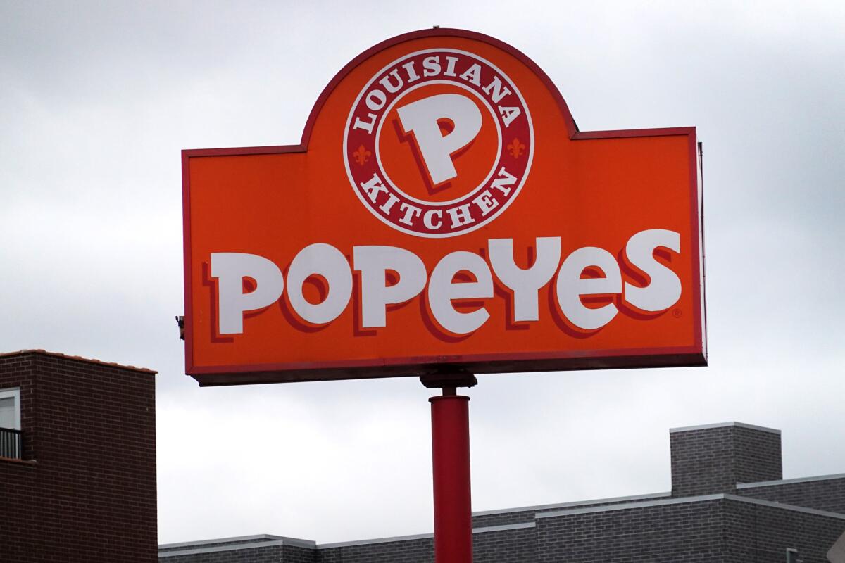 A Popeyes restaurant sign against a cloudy sky