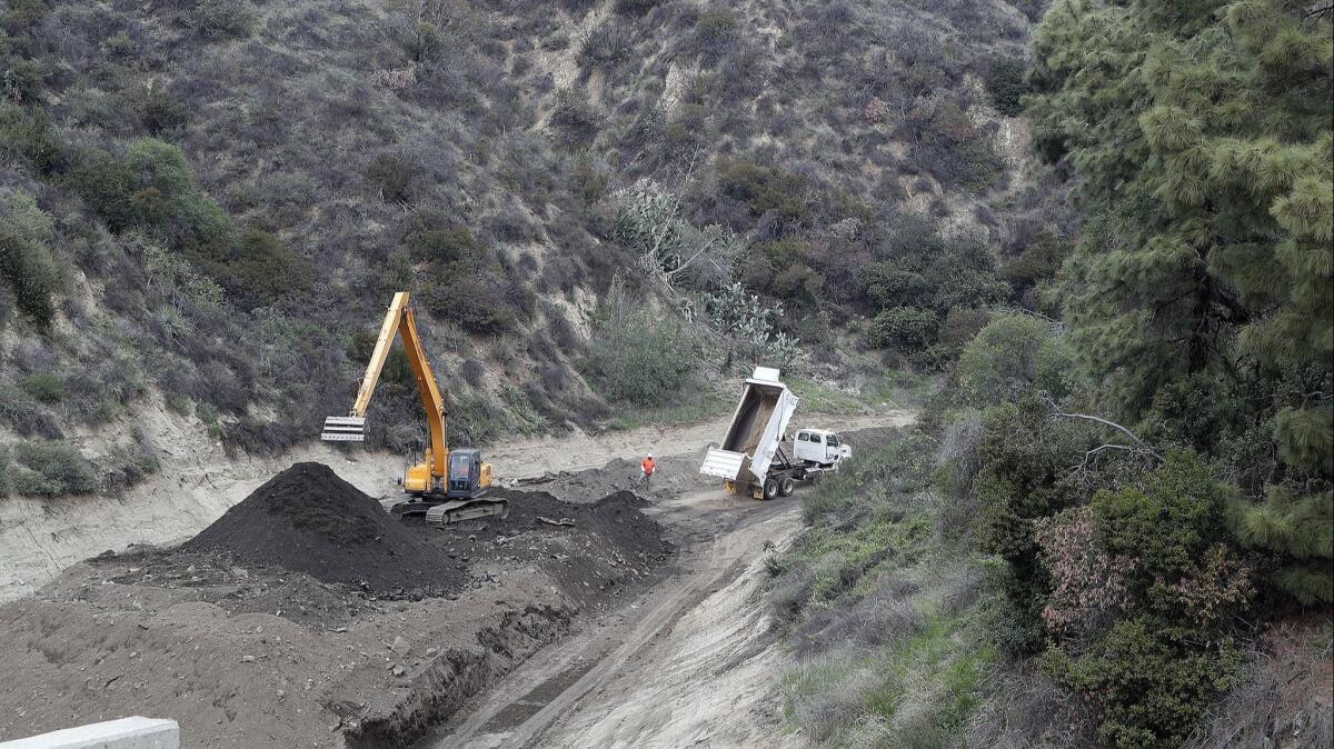 A large scoop moves dirt being dropped by a stream of dump trucks hauling debris from the Deer Debris Basin at the Sunset Debris Basin on Country Club Road in Burbank on Tuesday. This week's pending storms are likely to cause mudslides in burn areas.