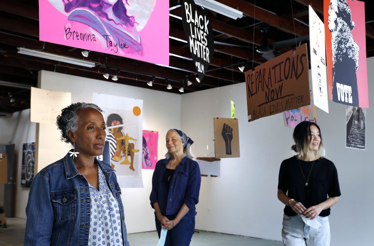 Brenda Thompson, Peggy Sivert and Tatum Hawkins, of SoLA Contemporary stand under protest signs suspended from the ceiling