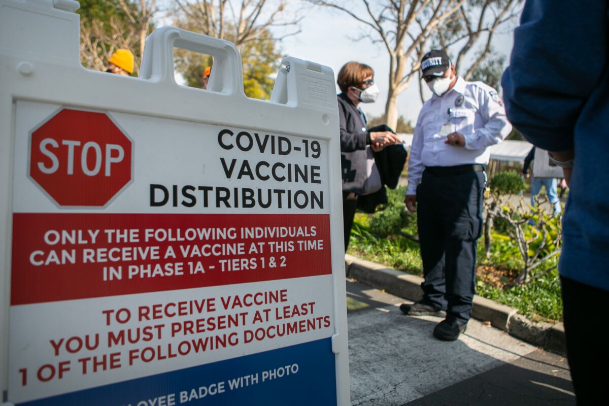 A woman stands next to a security officer near a sign with information about COVID-19 vaccine distribution.