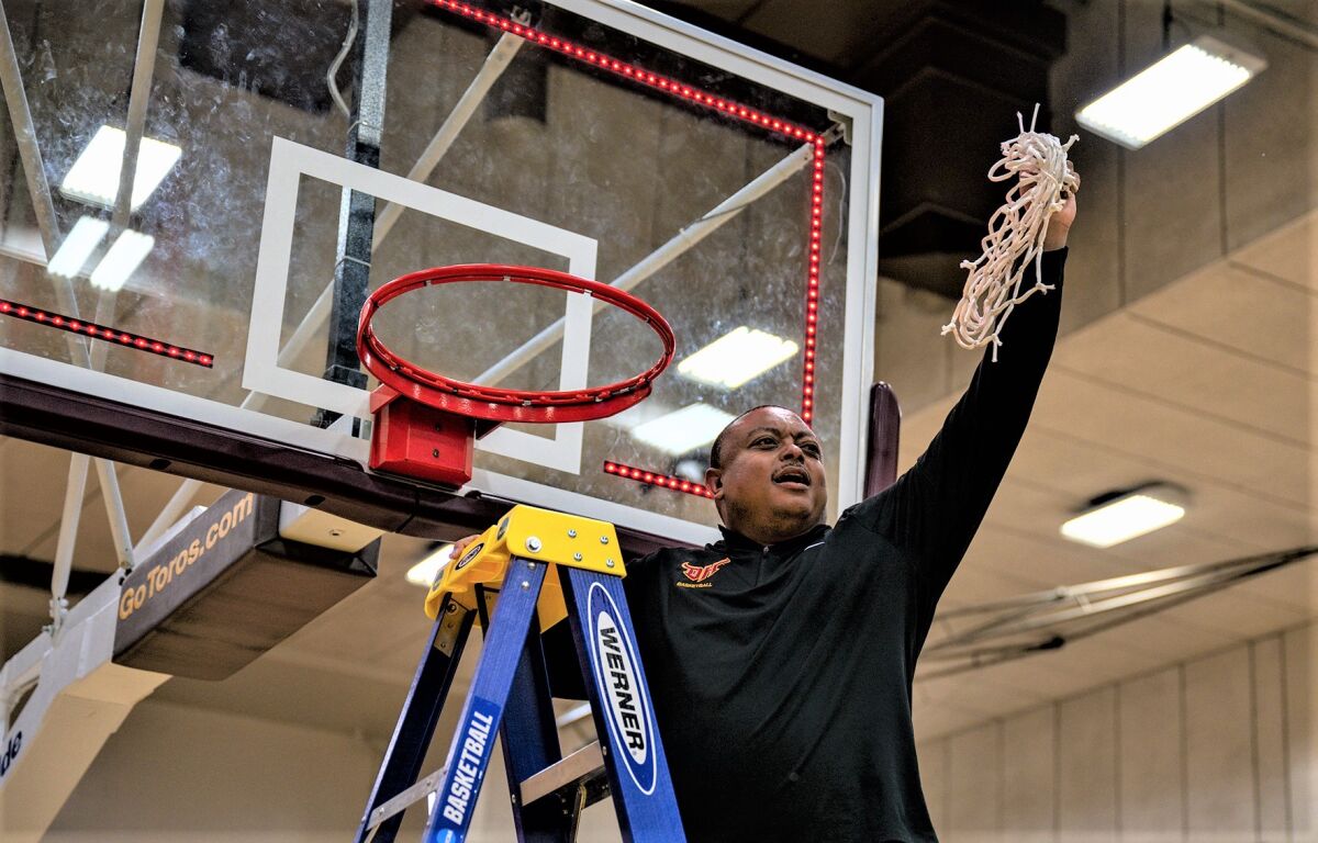 Cal State Dominguez Hills coach John Bonner stands on a ladder and holds up a net his team cut down.