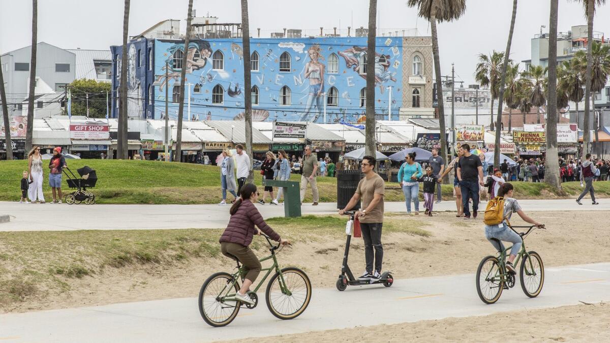 People ride bikes and scooters along the Venice Beach boardwalk on April 19, 2019.