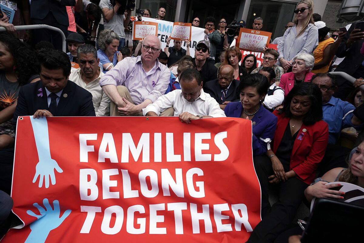 Protesters bow their heads while holding a red banner that says Families Belong Together