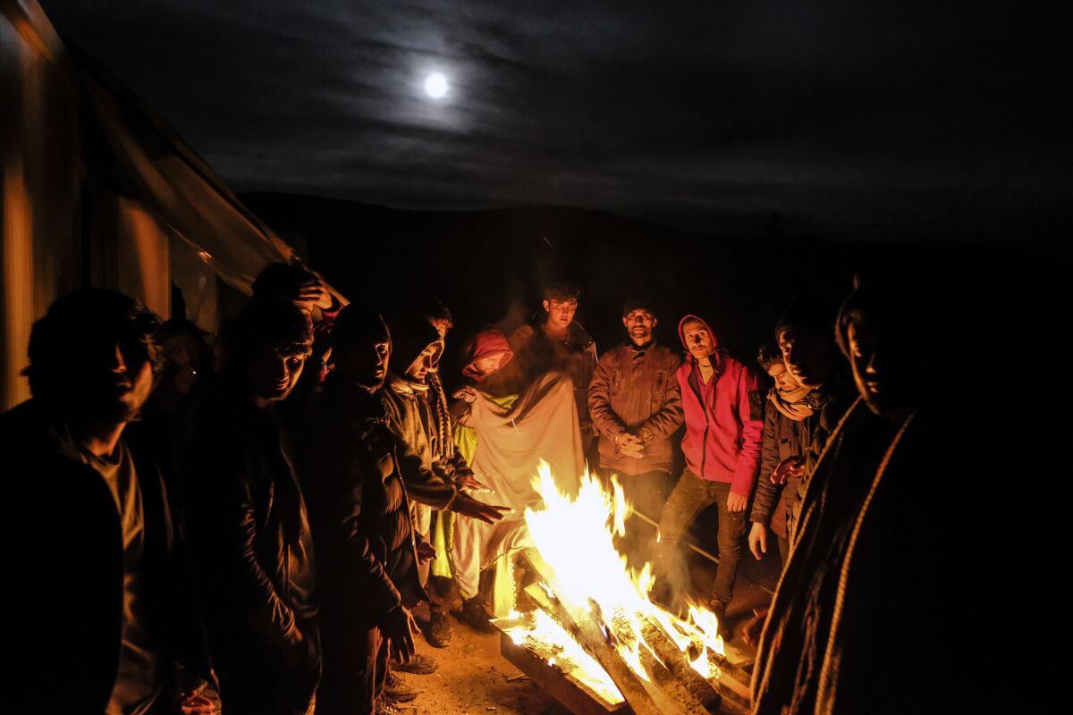 Migrants warm themselves around a fire at the Lipa camp outside Bihac, Bosnia, Wednesday, Dec. 30, 202, after hundreds failed to be relocated from the burnt-out tent camp in the northwest of the country. The migrants were supposed on Tuesday to be transferred from the much-criticized Lipa camp to a new location in the central part of the country, but have instead spent some 24 hours in buses before being told on Wednesday afternoon to disembark and return to the now empty camp site. (AP Photo/Kemal Softic)