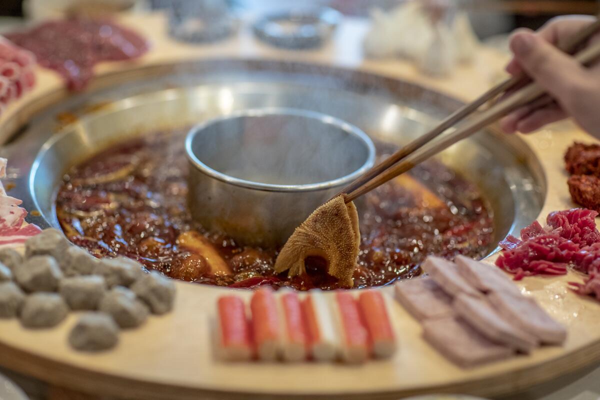 A diner dips tripe into spicy, bubbling soup base at Da Long Yi in San Gabriel.