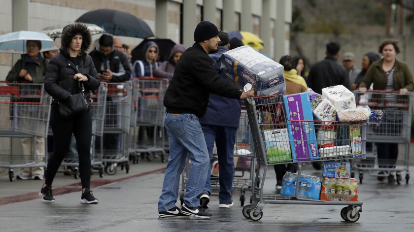 Costco customers roll groceries to their cars as others wait to enter the store on March 14, 2020, in San Leandro, Calif.