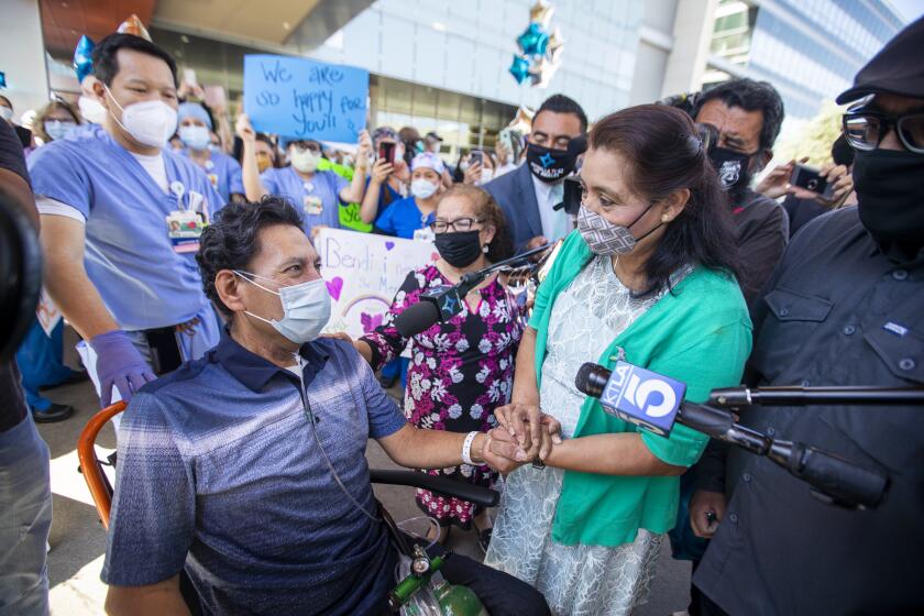 ORANGE, CA -- TUESDAY, MAY 5, 2020: Armando Mendoza, 53, of Anaheim, who was the hospital's second-ever COVID-19 patient, spent 45 days at St. Joseph Hospital, the longest local stint of any COVID-19 patients, holds his wife, Lilia Mendoza's hand, and greeted by this mother, Evangelina Mendoza, center, and son, David Mendoza, right, as he is released to his awaiting family with applause and salutes from hospital workers in Orange, CA, on May 5, 2020. Mendoza was healthy and had no underlying health conditions when he contracted the virus. (Allen J. Schaben / Los Angeles Times)