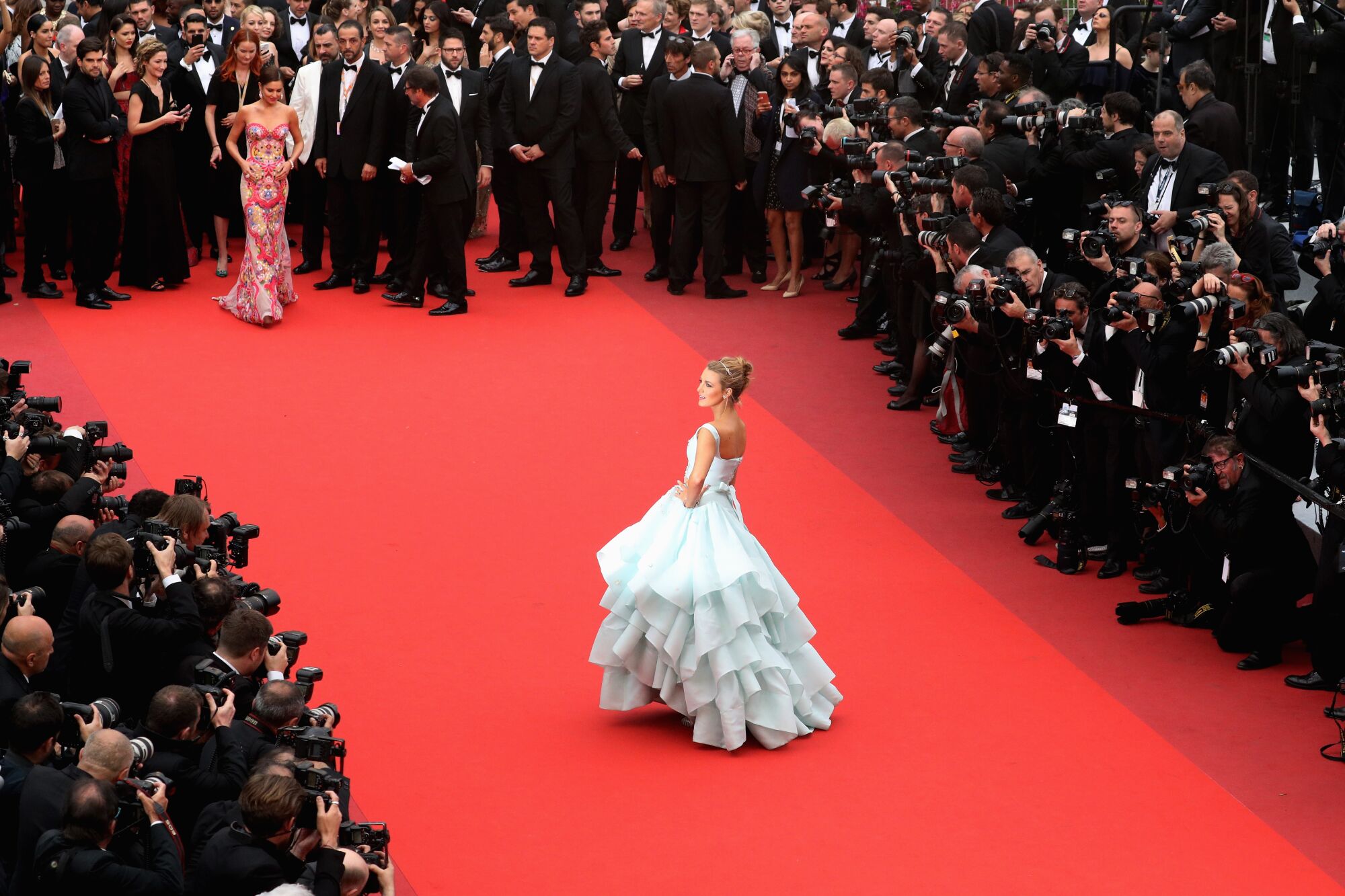 A woman in a flouncy light blue ball gown is the center of attention on a red carpet.