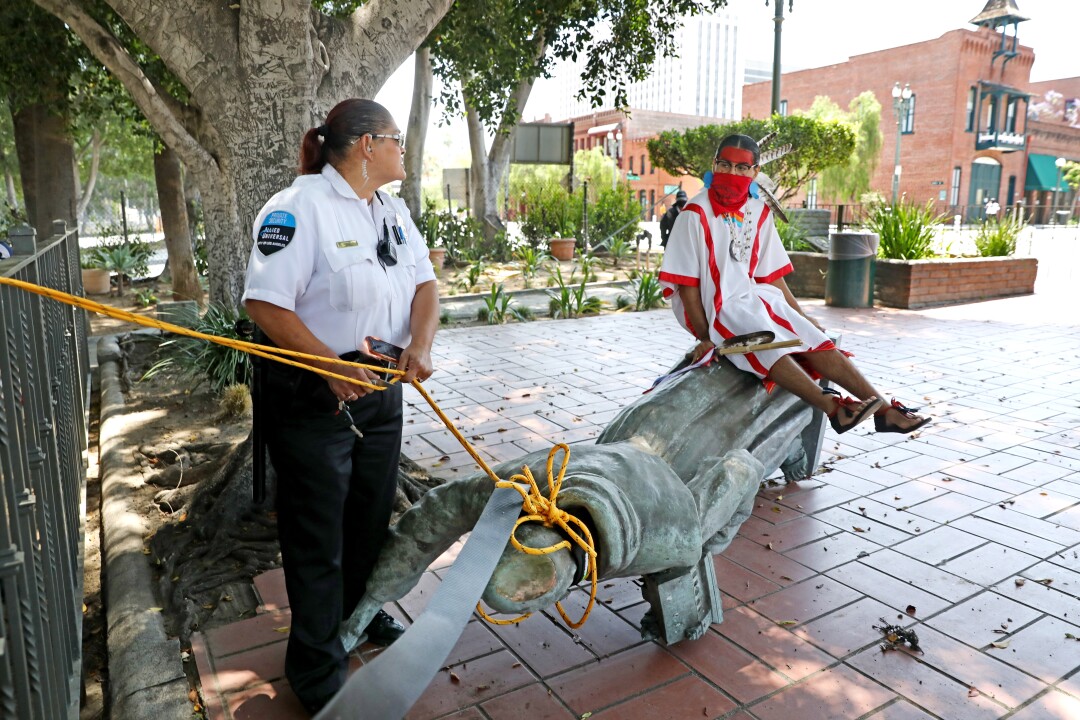 An activist sits atop a toppled statue of Junipero Serra in downtown L.A.