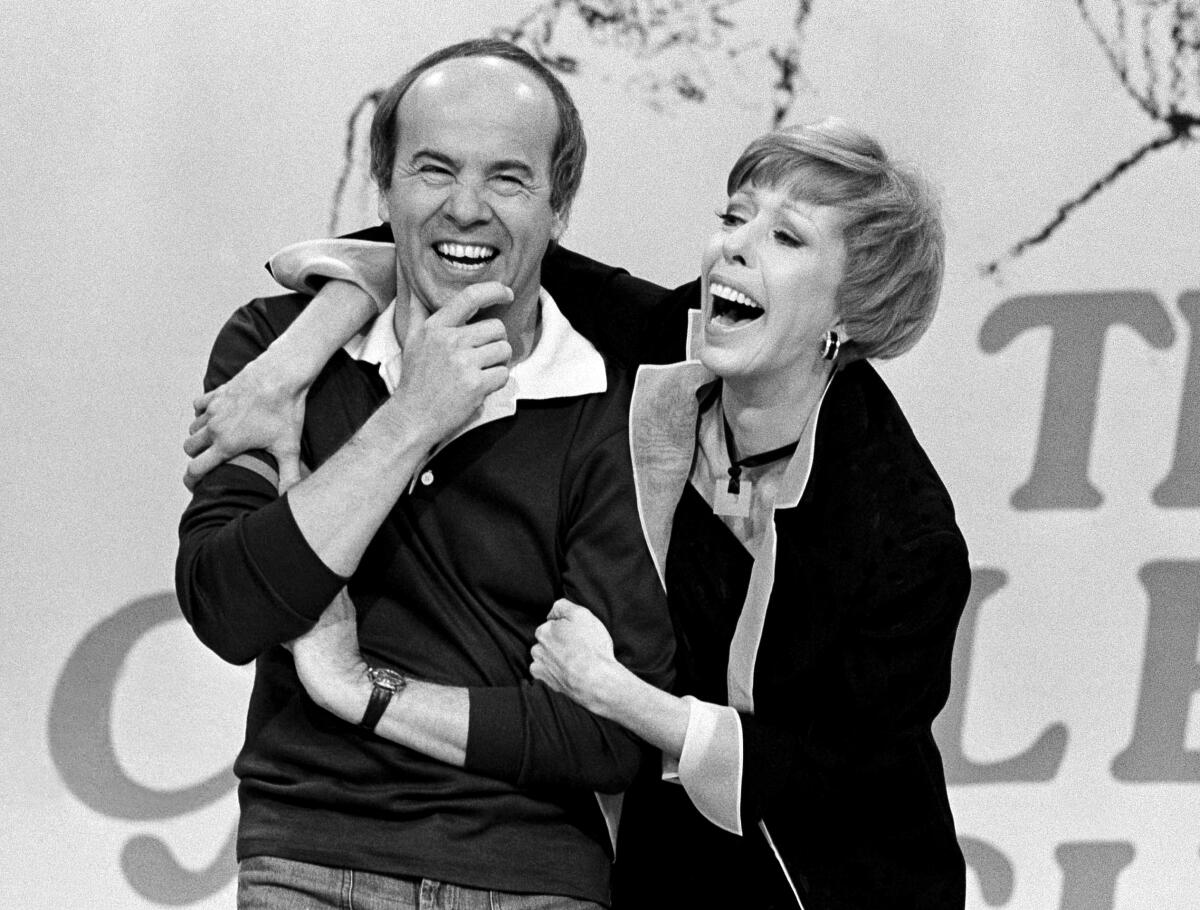 Tim Conway is embraced by Carol Burnett on a TV set.