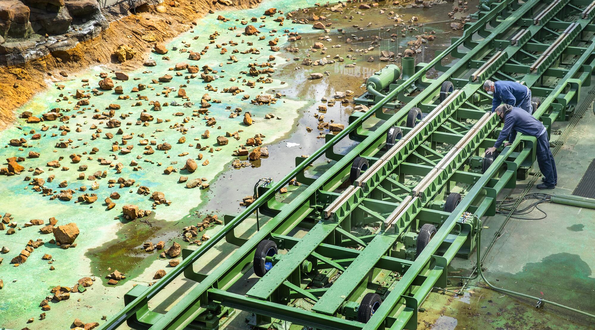 Two men in masks lean over a section of a theme park ride's track.