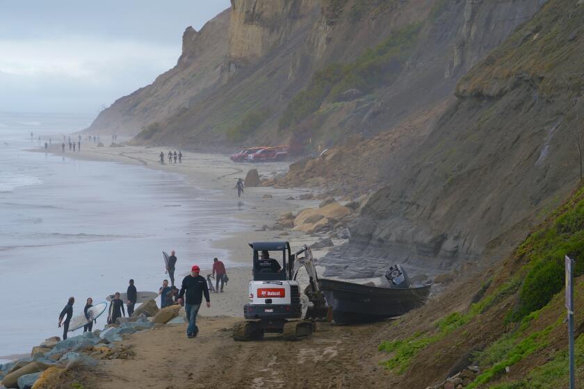 Surfers walk past a salvage crew beginning to haul a panga on March 12, 2023